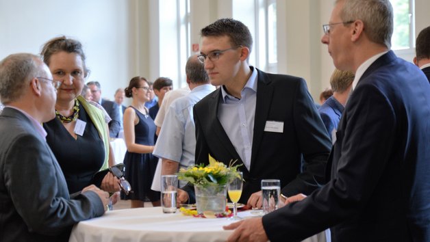 Vier Menschen stehen an einem runden Tisch und reden über etwas